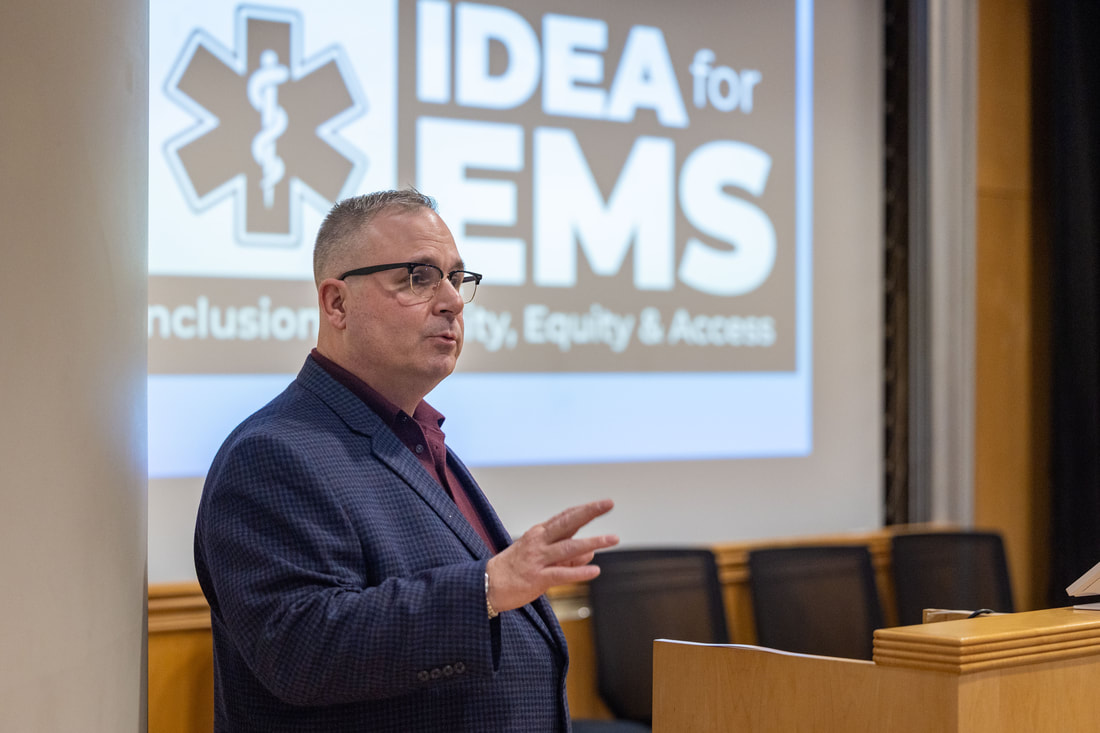A presenter speaks beside a projected EMS education slide at the March 2025 symposium.